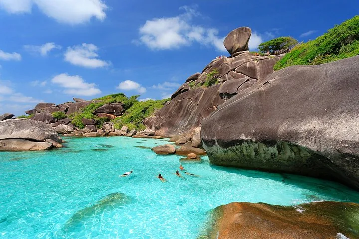 Personnes nageant dans une eau turquoise limpide près de gros rochers